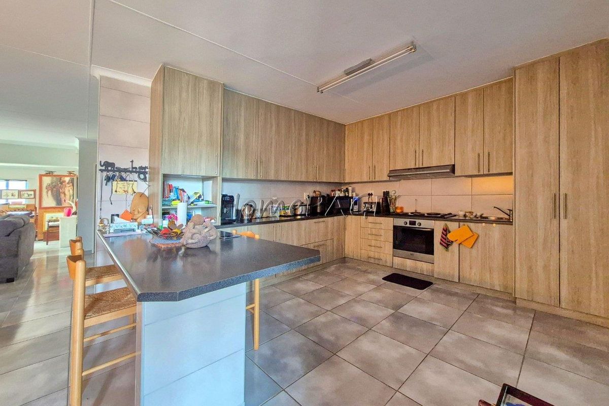 A functional kitchen featuring wood-look cabinetry, a central island, built-in oven, extractor fan, and tiled flooring, offering ample storage and workspace.