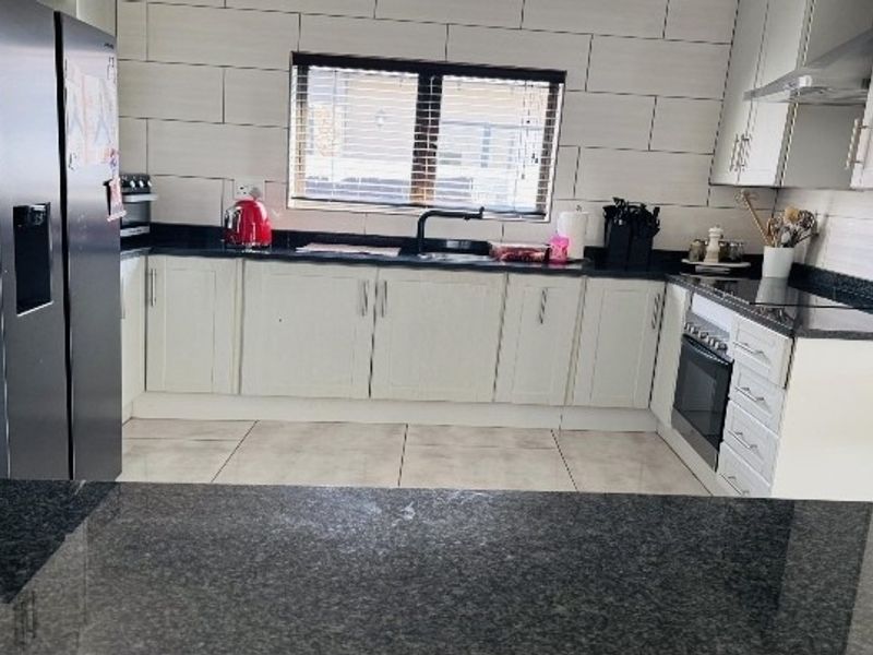 A well-maintained kitchen featuring white cabinetry, dark granite countertops, a built-in oven, extractor fan, and a tiled backsplash.