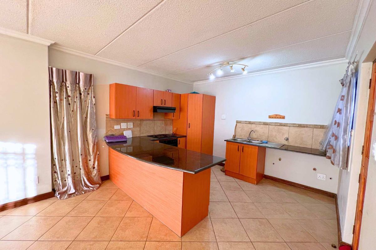 A functional kitchen featuring orange-toned cabinetry, dark granite countertops, tiled backsplash, and tiled flooring, offering a practical layout for daily meal preparation.