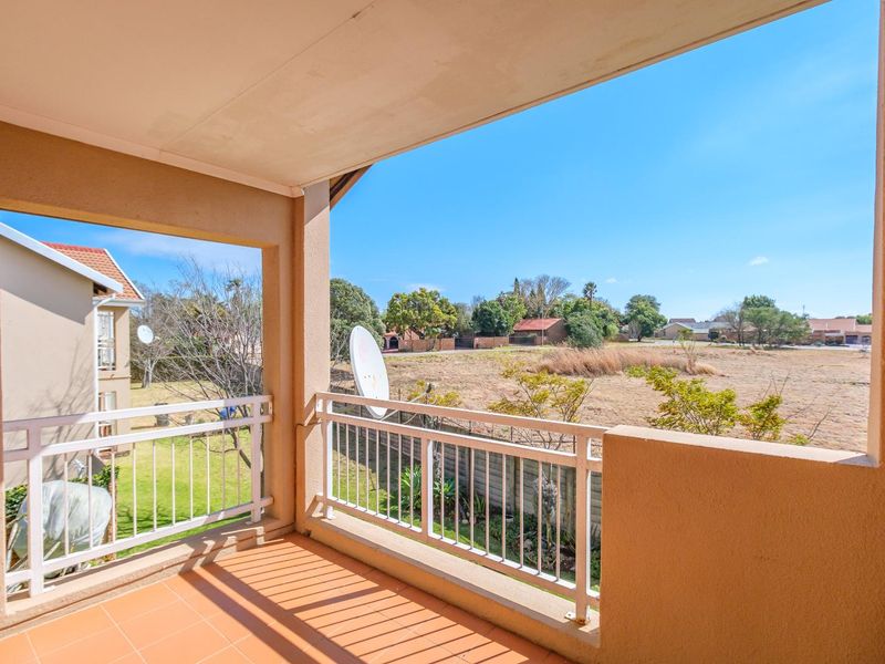 A covered balcony featuring tiled flooring and a metal balustrade, offering an open view of the surrounding neighborhood and landscape.