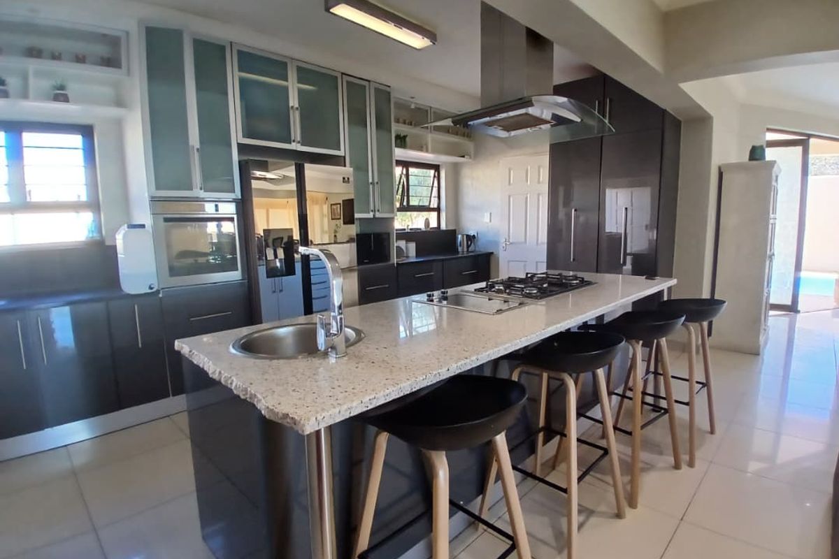 Modern kitchen featuring a central island with a built-in gas hob, stone countertops, sleek cabinetry, and a stainless steel extractor fan.