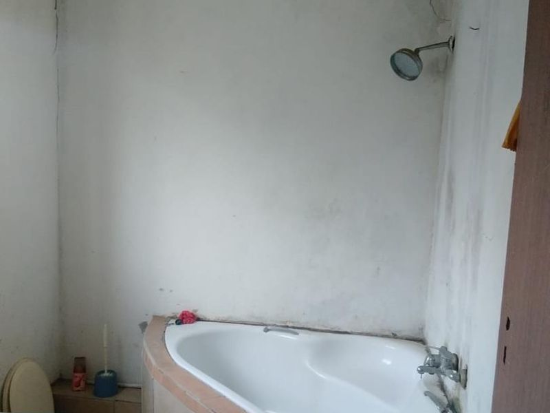 A dated bathroom featuring a corner bathtub with tiled surround, a shower head, and a toilet, requiring significant cosmetic renovation and wall repairs.