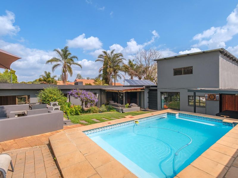A well-maintained outdoor entertainment area featuring a swimming pool, paved patio, built-in braai, and landscaped garden with solar panels on the roof.