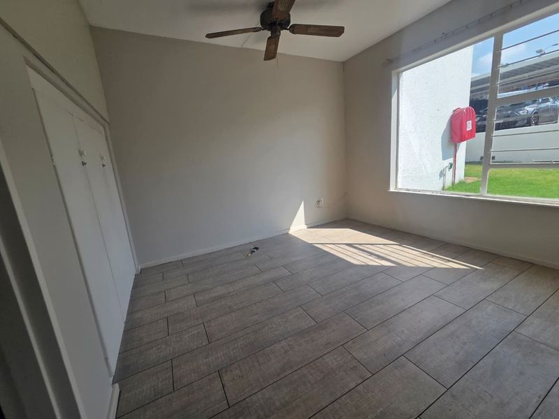 A bright, empty bedroom featuring modern wood-look tiled flooring, a ceiling fan, and built-in cupboards, offering a clean canvas for personalization.