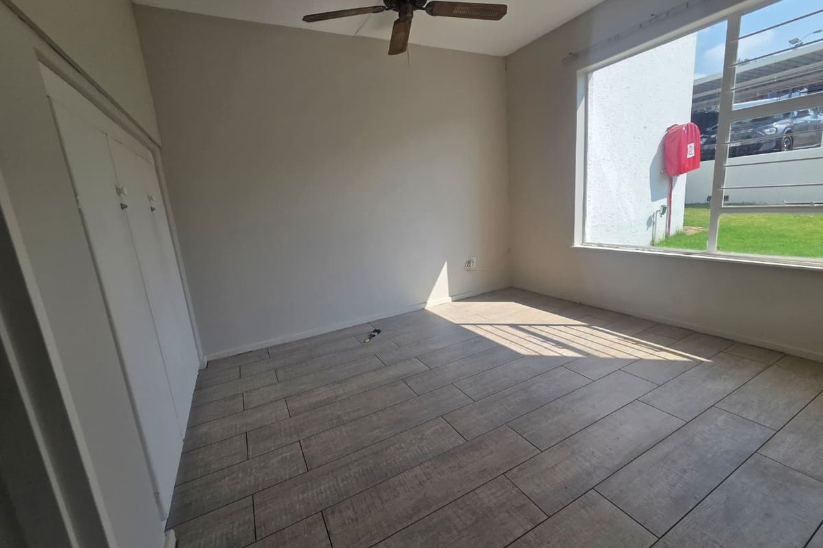 A bright, empty bedroom featuring modern wood-look tiled flooring, a ceiling fan, and built-in cupboards, offering a clean canvas for personalization.
