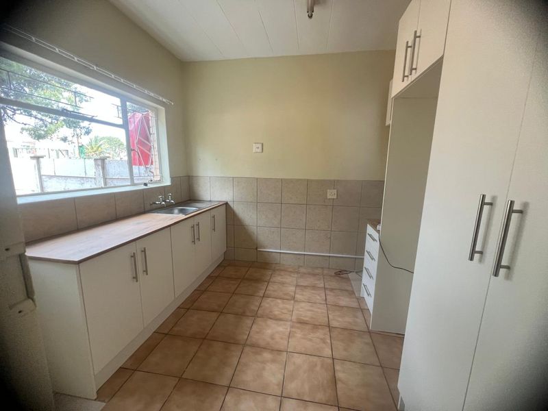 A functional, empty kitchen featuring built-in white cabinetry, tiled flooring, a stainless steel sink, and ample storage space with a built-in pantry.