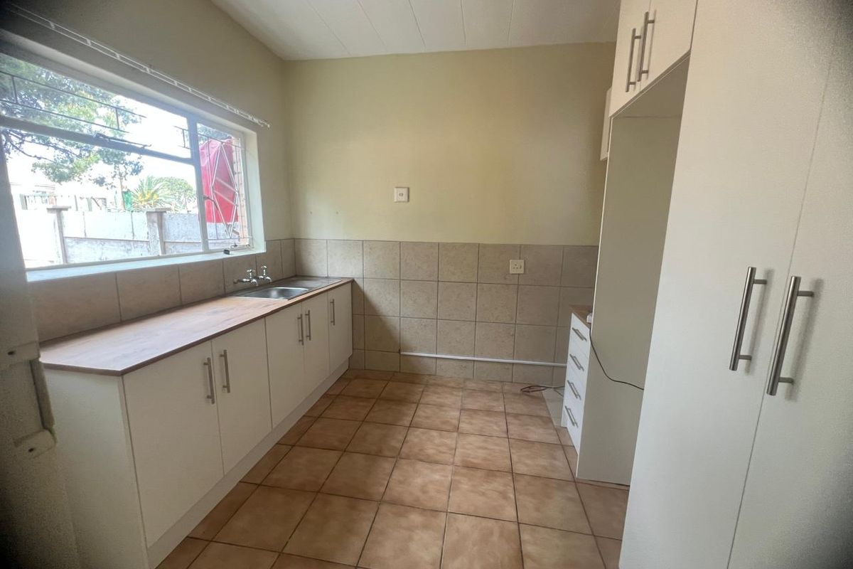A functional, empty kitchen featuring built-in white cabinetry, tiled flooring, a stainless steel sink, and ample storage space with a built-in pantry.