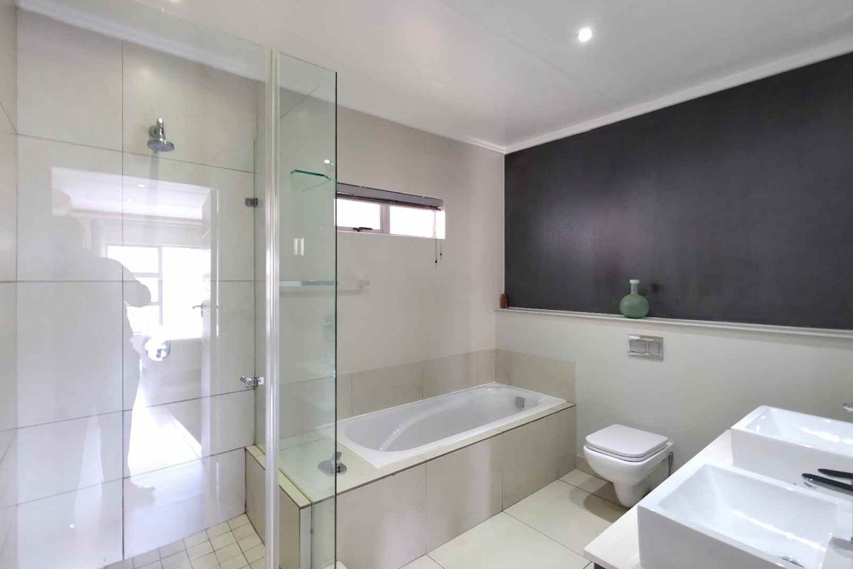 Modern bathroom featuring a glass-enclosed shower, a built-in bathtub, a wall-mounted toilet, and a double vanity with contemporary fixtures.