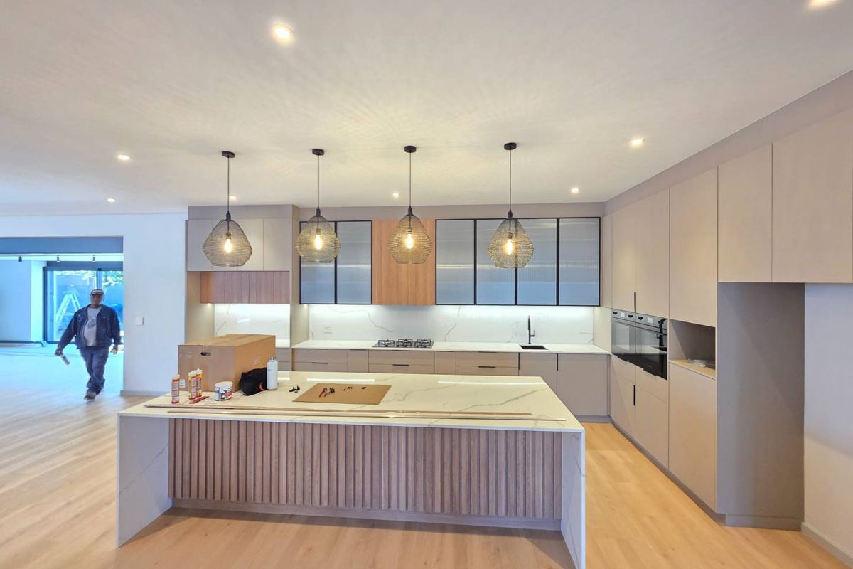 Modern, newly installed kitchen featuring a large stone-topped island, integrated cabinetry, built-in appliances, and contemporary timber slat detailing.