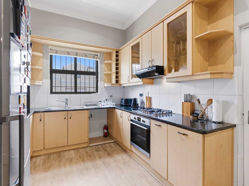 A functional kitchen featuring light wood cabinetry, granite countertops, a gas hob, built-in oven, and a tiled backsplash with ample storage space.
