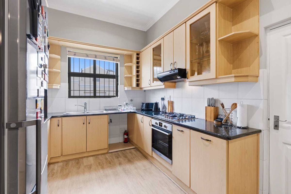 A functional kitchen featuring light wood cabinetry, granite countertops, a gas hob, built-in oven, and a tiled backsplash with ample storage space.