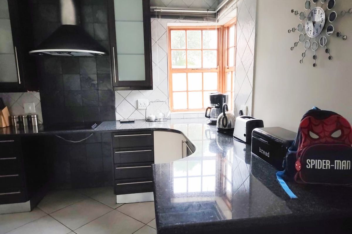 A functional kitchen featuring dark cabinetry, granite countertops, a built-in extractor fan, and tiled splashbacks with a window providing natural light.