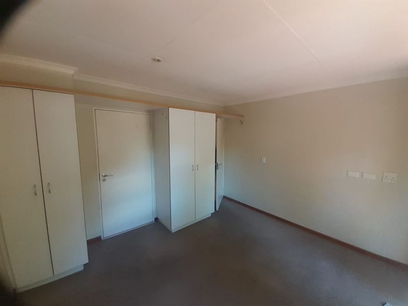 A clean, empty bedroom featuring neutral walls, carpeted flooring, and built-in storage cupboards, providing a versatile space ready for personalization.
