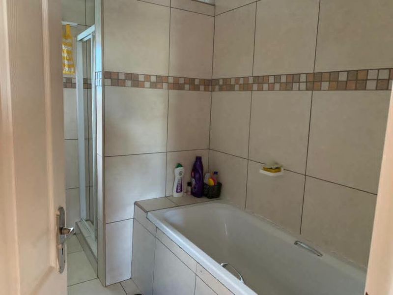 A functional bathroom featuring a built-in bathtub, a separate shower enclosure, and neutral ceramic wall and floor tiling.