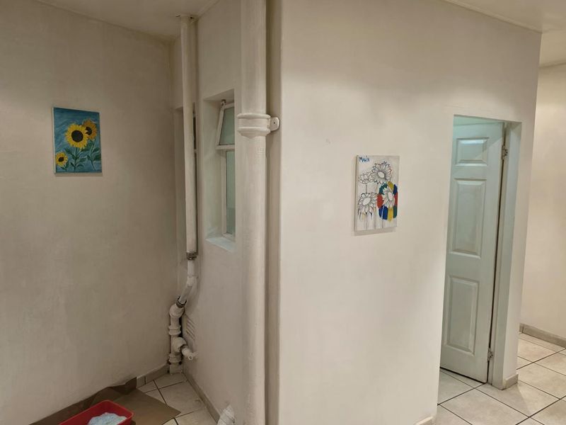 A functional hallway area featuring tiled flooring and exposed plumbing infrastructure, providing access to adjacent rooms within the apartment.