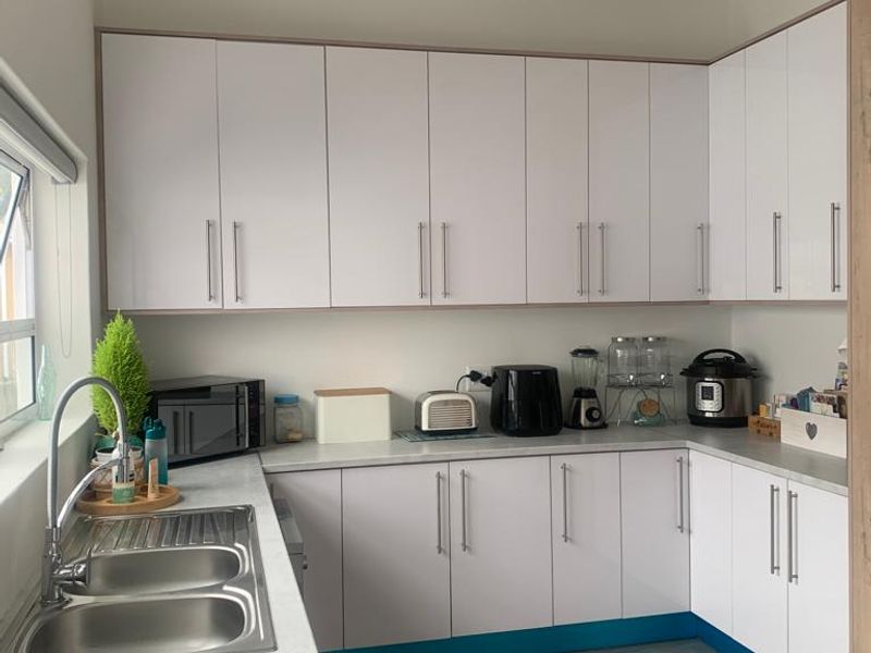 A functional kitchen featuring white built-in cabinetry, laminate countertops, a stainless steel double sink, and tiled flooring with ample storage space.