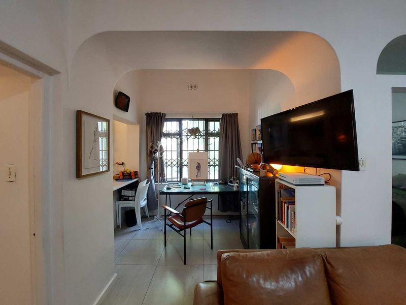 A living area featuring an arched transition to a study nook with a built-in desk and security-barred windows.