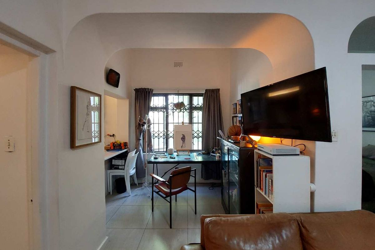 A living area featuring an arched transition to a study nook with a built-in desk and security-barred windows.
