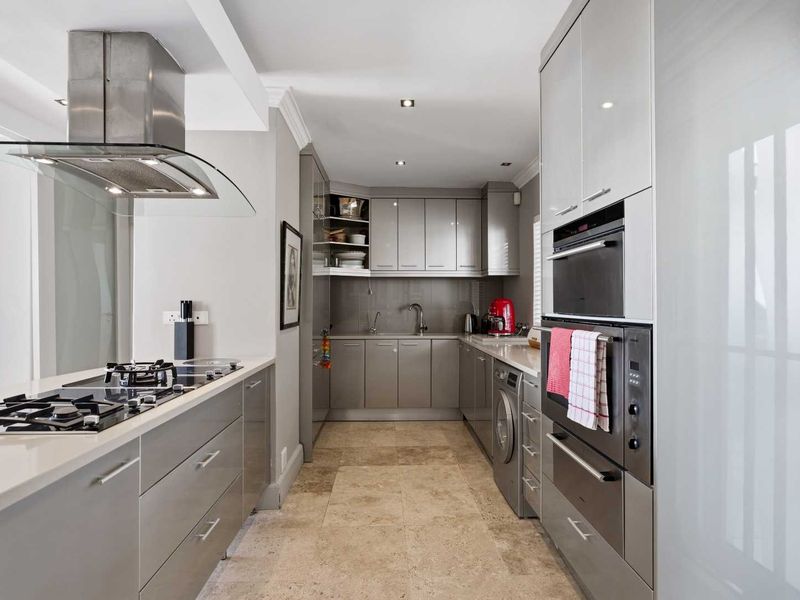 Modern kitchen featuring sleek grey cabinetry, stone countertops, high-end built-in appliances, gas hob, and durable tiled flooring.