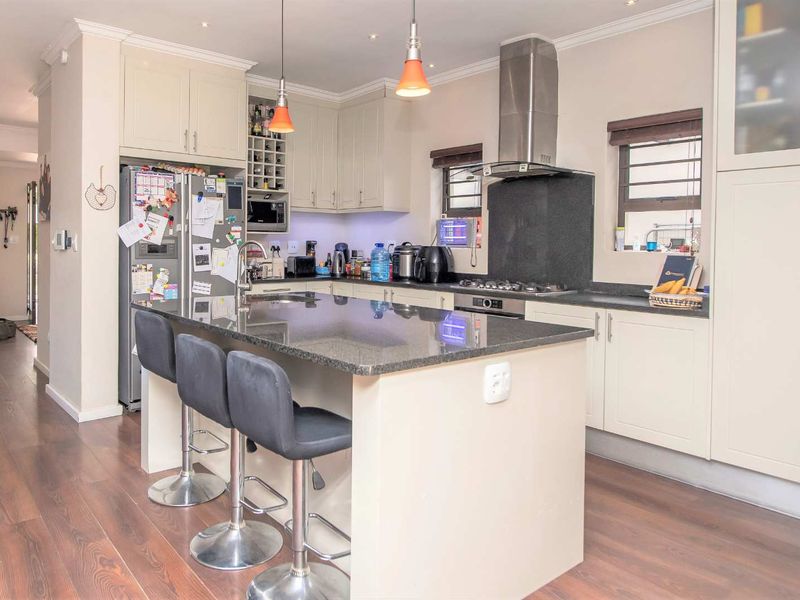 Modern kitchen featuring a central island with granite countertops, ample built-in cabinetry, stainless steel appliances, and high-quality laminate flooring.