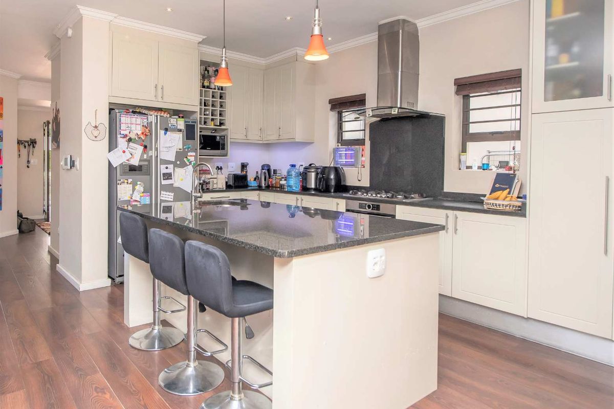 Modern kitchen featuring a central island with granite countertops, ample built-in cabinetry, stainless steel appliances, and high-quality laminate flooring.