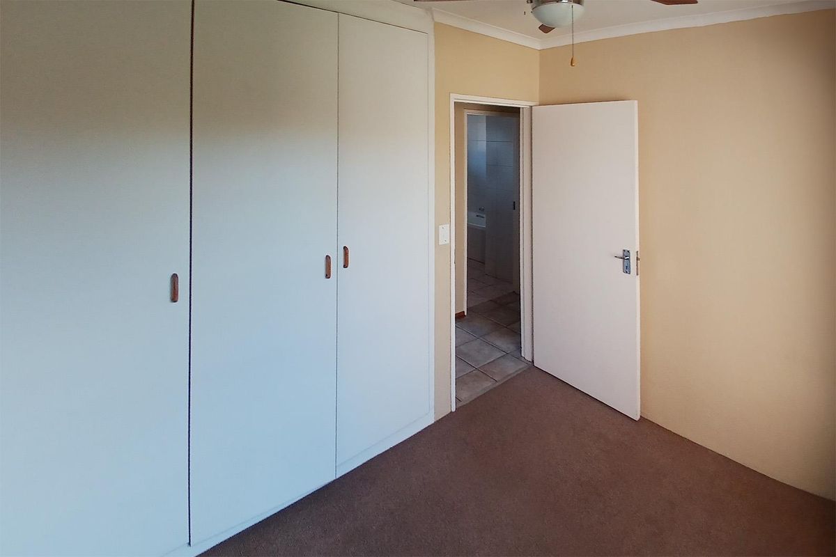 A vacant bedroom featuring built-in cupboards, carpeted flooring, and a ceiling fan, with direct access to an adjacent bathroom.