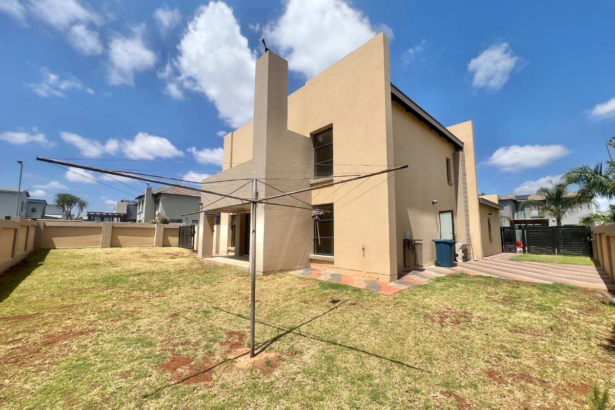 Rear view of the double-story house featuring a paved patio area, exterior chimney stack, and a spacious private garden with perimeter walling.