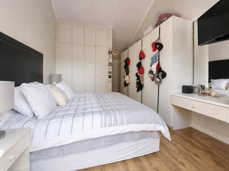A bedroom featuring extensive built-in cupboard storage, laminate flooring, and a built-in vanity unit with a mirror.