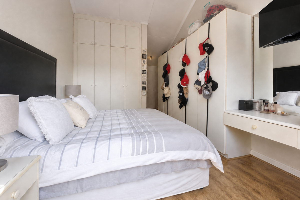 A bedroom featuring extensive built-in cupboard storage, laminate flooring, and a built-in vanity unit with a mirror.