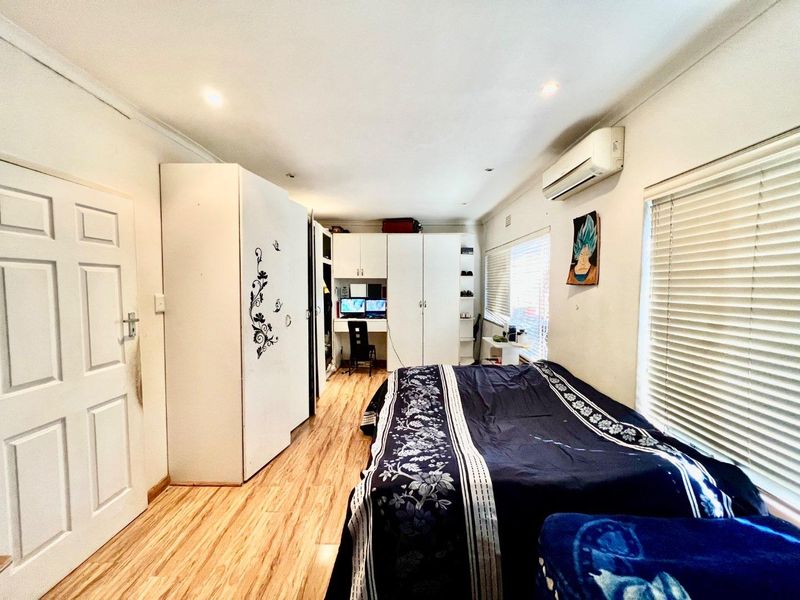 A well-lit bedroom featuring laminate flooring, built-in storage cabinetry, and a wall-mounted split-system air conditioning unit.