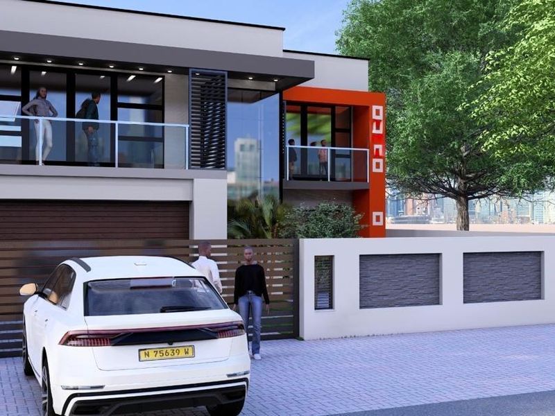 Modern two-story residential facade featuring clean lines, upper-level balconies with glass balustrades, and a secure gated entrance with a paved driveway.