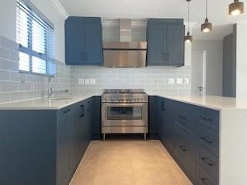 Modern kitchen featuring dark blue cabinetry, stone countertops, subway tile backsplash, and stainless steel appliances, including a built-in oven and extractor fan.