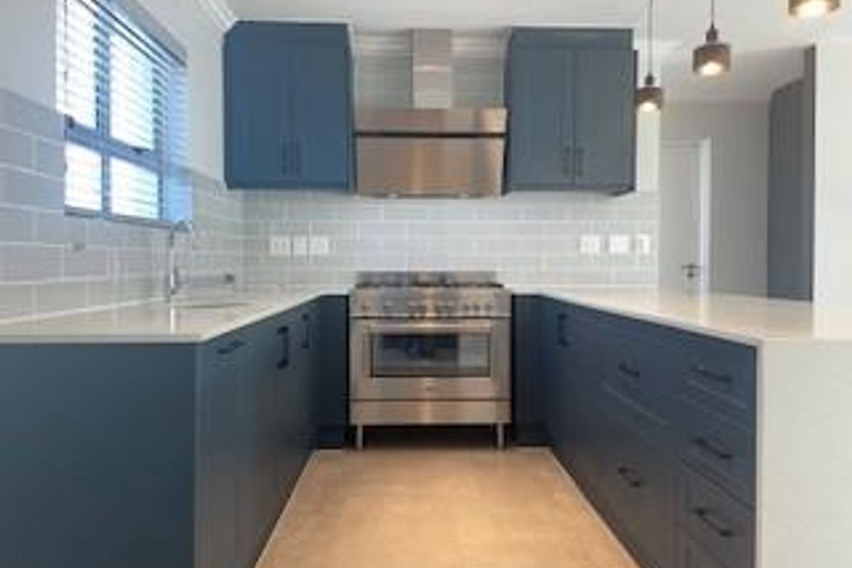 Modern kitchen featuring dark blue cabinetry, stone countertops, subway tile backsplash, and stainless steel appliances, including a built-in oven and extractor fan.