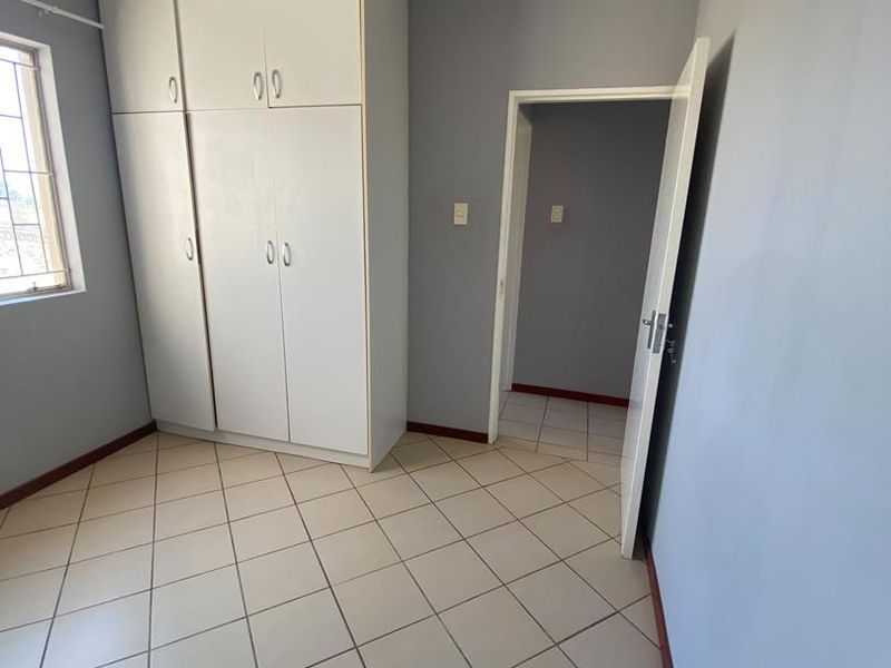 A vacant bedroom featuring tiled flooring, built-in cupboards, and neutral grey walls, offering a clean canvas for personalization.