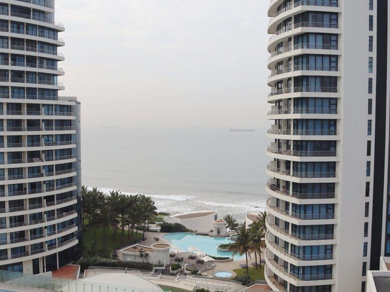 Elevated view overlooking the ocean, featuring modern high-rise apartment towers and a communal swimming pool area below.