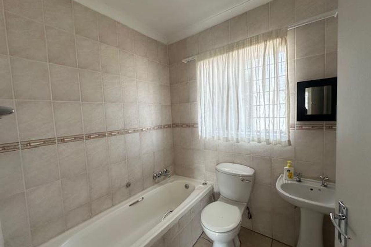 A functional bathroom featuring a standard bathtub, pedestal basin, and toilet with neutral wall tiling throughout.