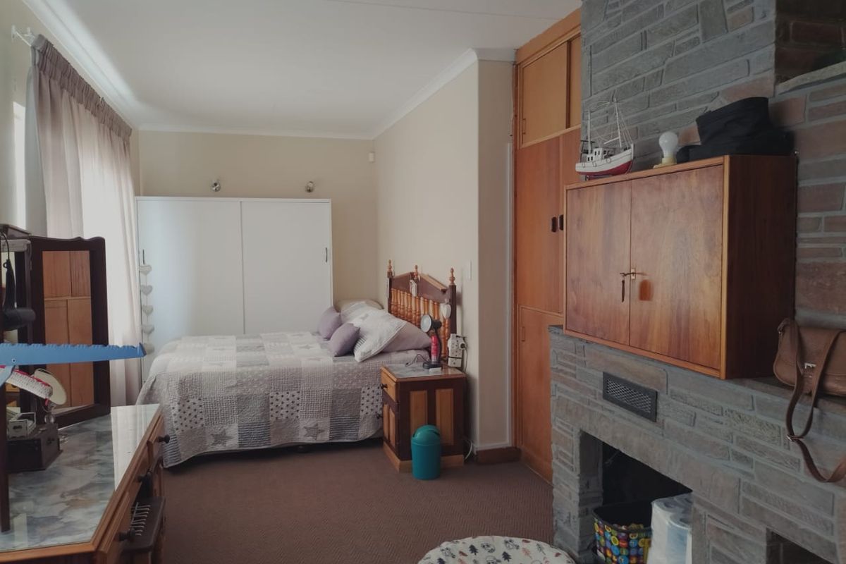 A bedroom featuring a stone-clad fireplace, built-in wooden cabinetry, and carpeted flooring.