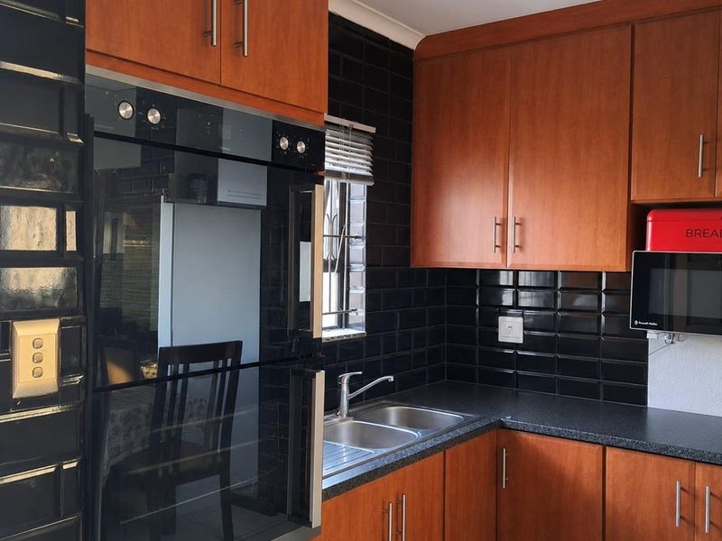 A functional kitchen featuring wood-finish cabinetry, dark subway tile backsplash, integrated oven, and a double bowl stainless steel sink with modern mixer tap.