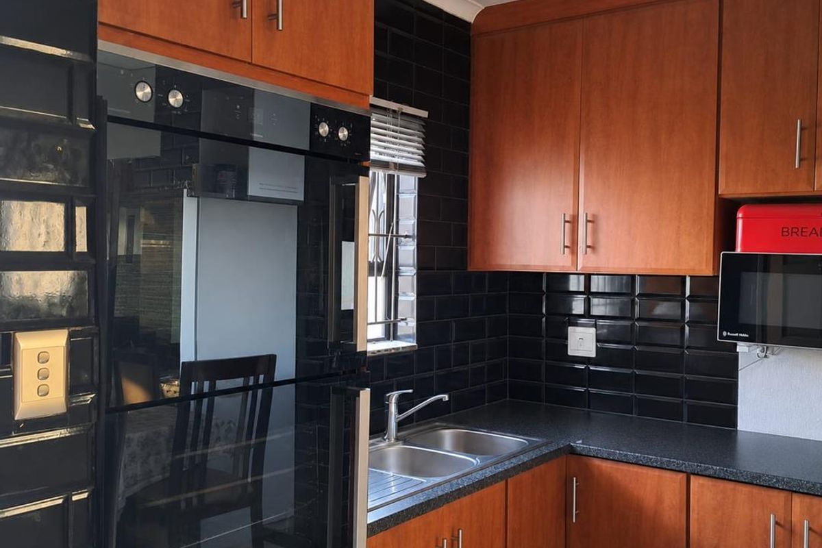 A functional kitchen featuring wood-finish cabinetry, dark subway tile backsplash, integrated oven, and a double bowl stainless steel sink with modern mixer tap.