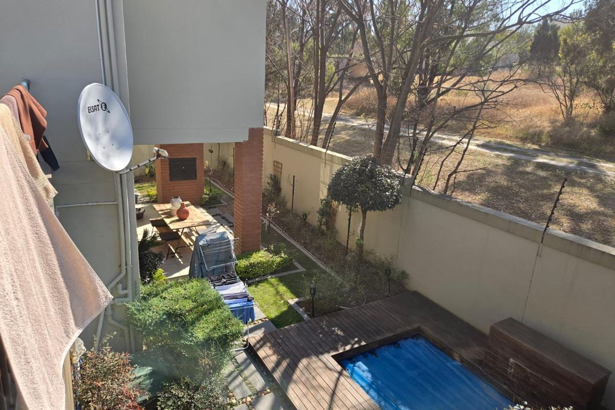 Rear garden area featuring a small swimming pool with wooden decking, a covered patio with a built-in braai, and perimeter walling.