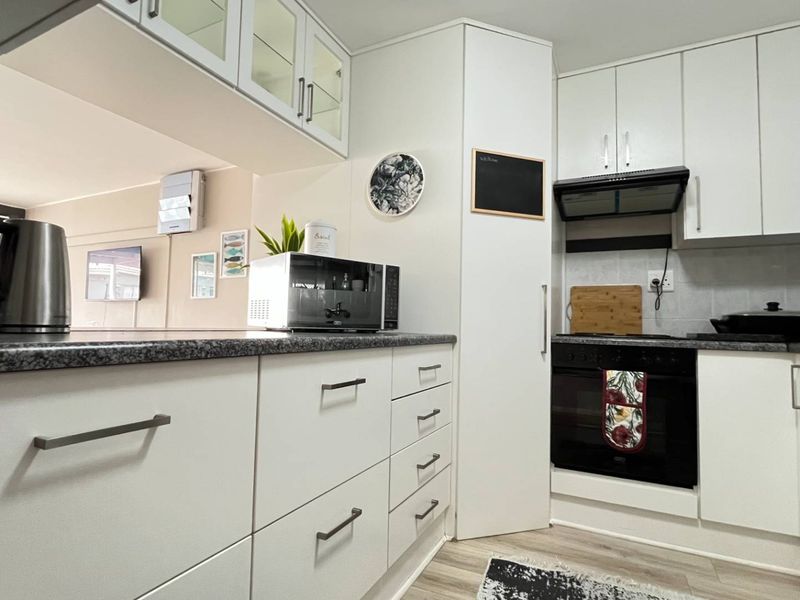 A clean, modern kitchen featuring white cabinetry, dark laminate countertops, and integrated appliances, offering a functional and well-maintained cooking space.