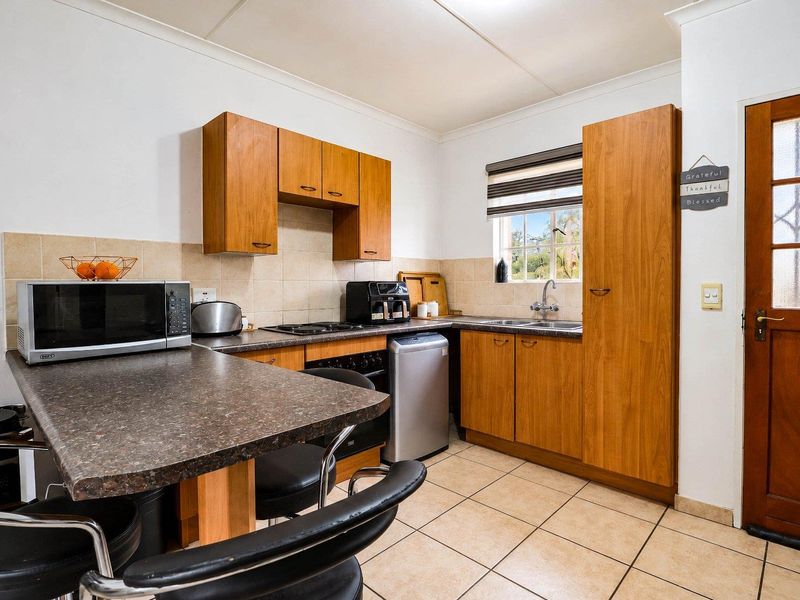 A functional kitchen featuring wood-look cabinetry, laminate countertops, tiled backsplash, and ceramic flooring, providing a practical workspace with integrated cooking and cleaning facilities.