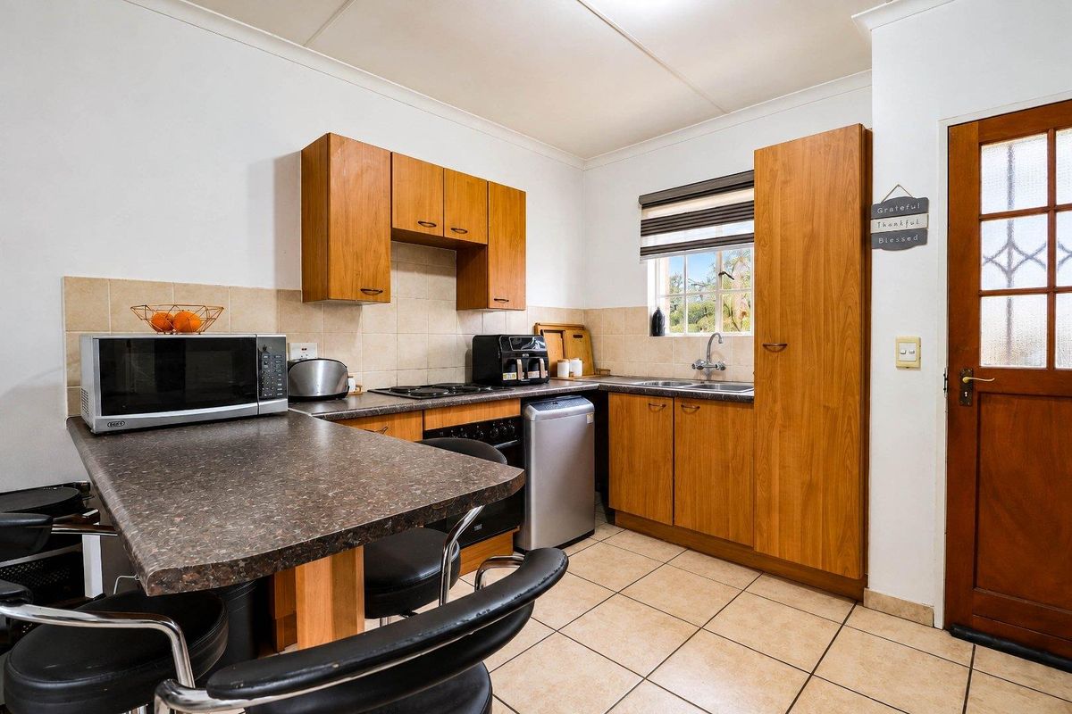 A functional kitchen featuring wood-look cabinetry, laminate countertops, tiled backsplash, and ceramic flooring, providing a practical workspace with integrated cooking and cleaning facilities.
