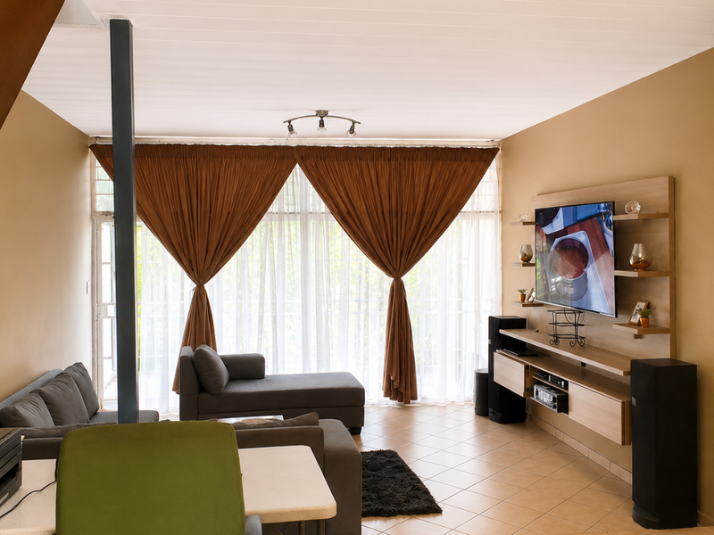 A living room featuring tiled flooring, a built-in media console, and large windows with curtains leading to an outdoor area.