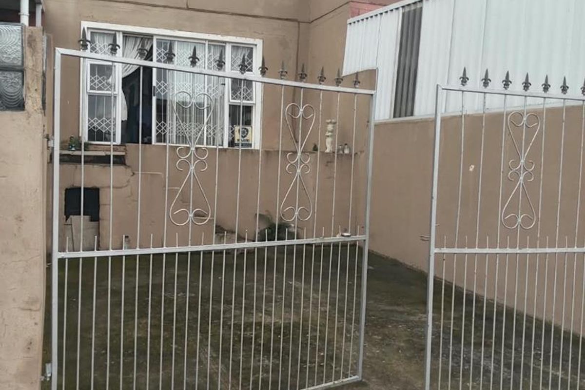 Rear exterior view of the apartment featuring a paved courtyard area, metal security gate, and multi-story building facade with visible wear.