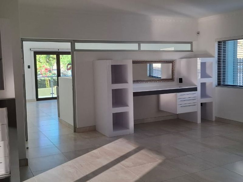 Spacious bedroom featuring neutral tiled flooring, built-in desk and shelving units, split-system air conditioning, and large windows with venetian blinds.