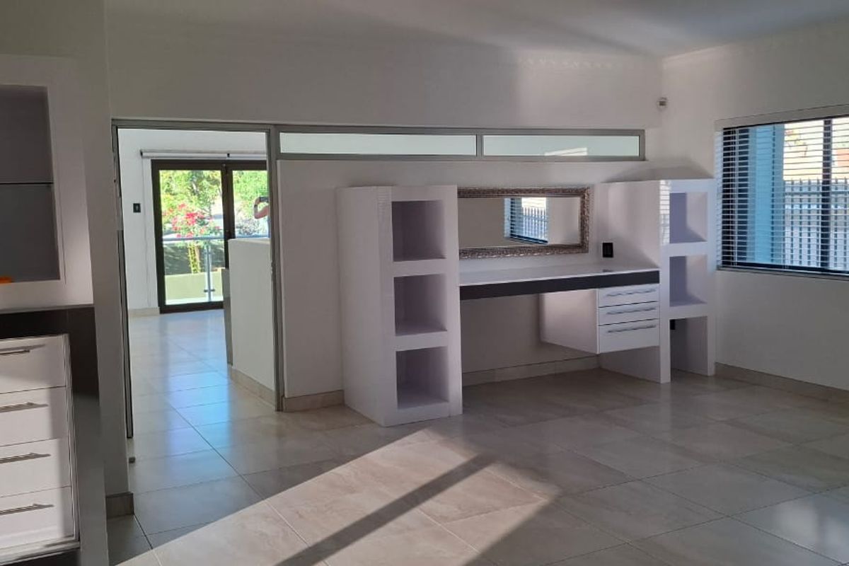 Spacious bedroom featuring neutral tiled flooring, built-in desk and shelving units, split-system air conditioning, and large windows with venetian blinds.