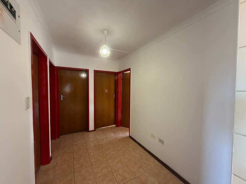 A functional, empty hallway featuring tiled flooring, cove cornicing, and multiple timber doors with red-painted frames.