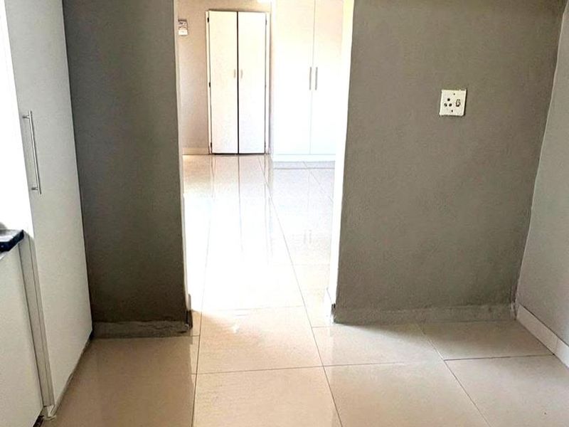 A bright, tiled hallway connecting two rooms, featuring built-in storage cupboards and neutral wall finishes.