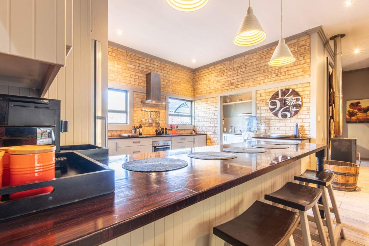 Spacious kitchen featuring a large wooden breakfast bar, exposed brick walls, stainless steel extractor fan, and integrated cabinetry with modern lighting.